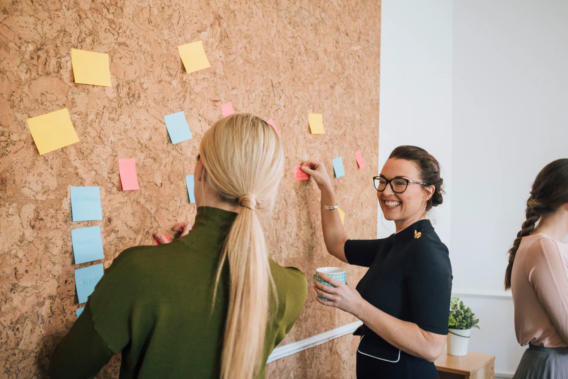 two women putting post it notes on board workplace meeting