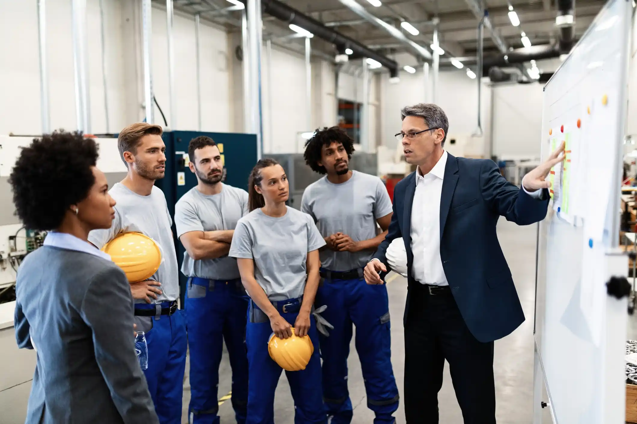 Mature businessman explaining new strategy plans to group of employees in a factory