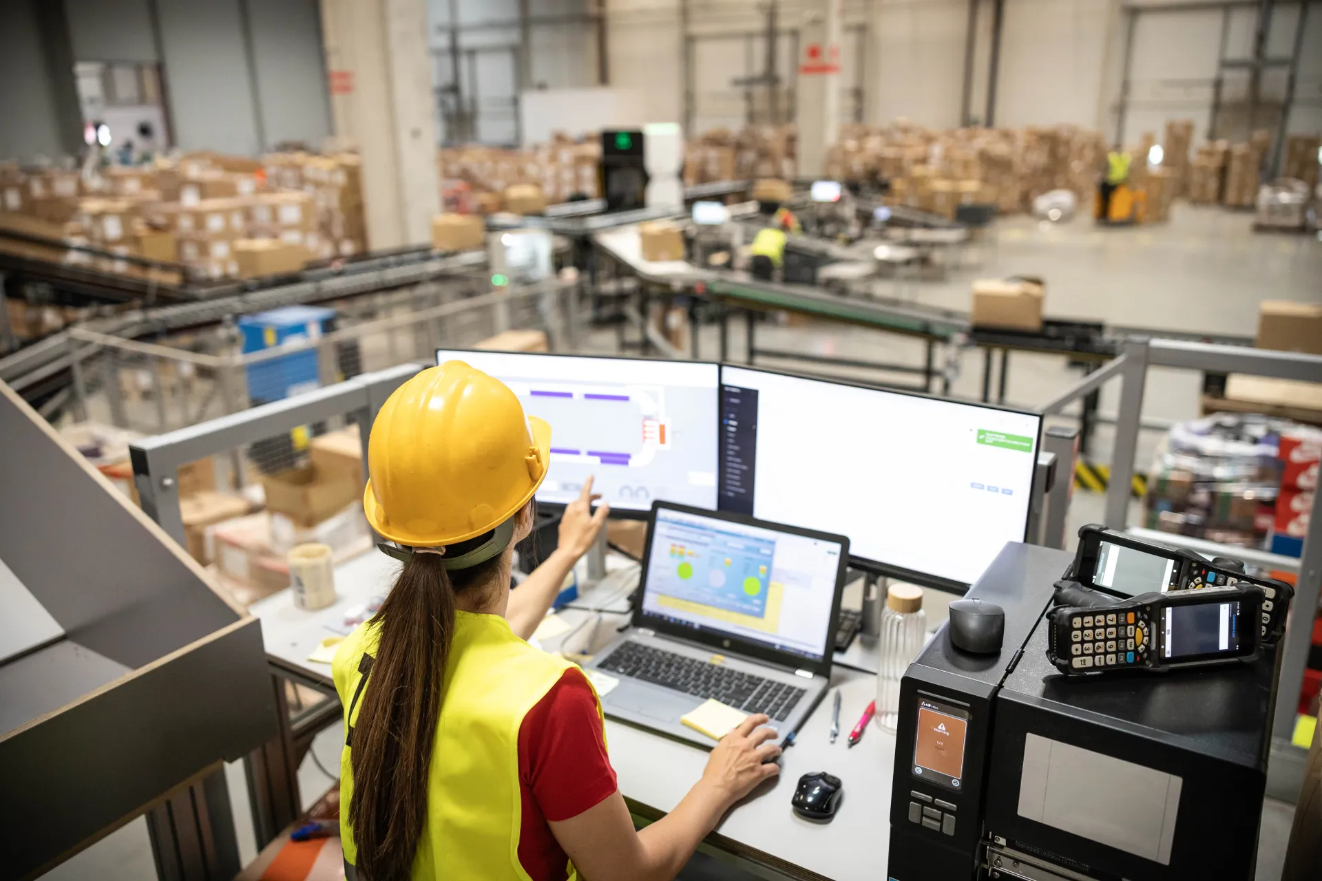 Worker wearing hard hat checking computer screen near conveyor belt
