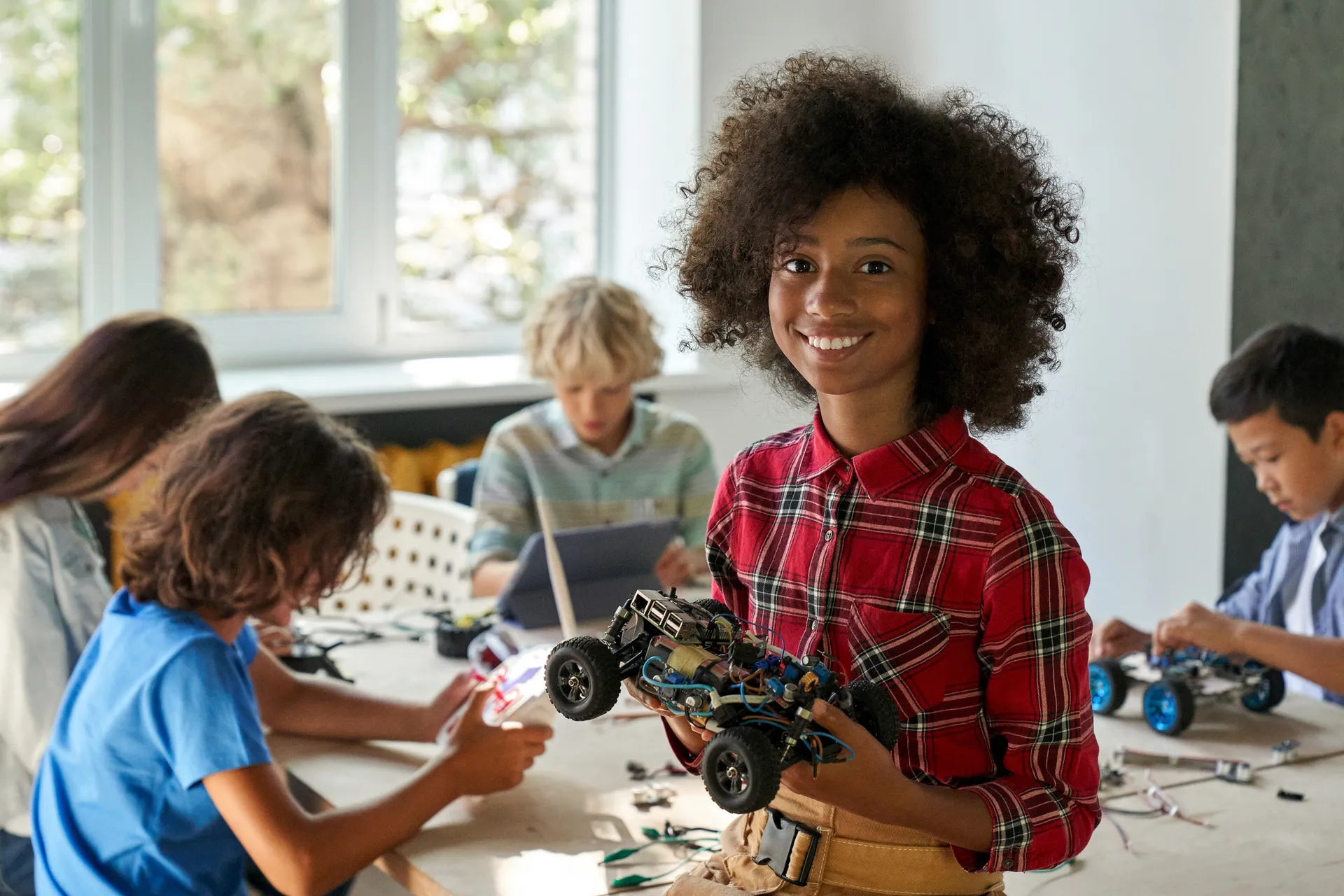 Female school kid holding robotic car looking at camera at STEM class