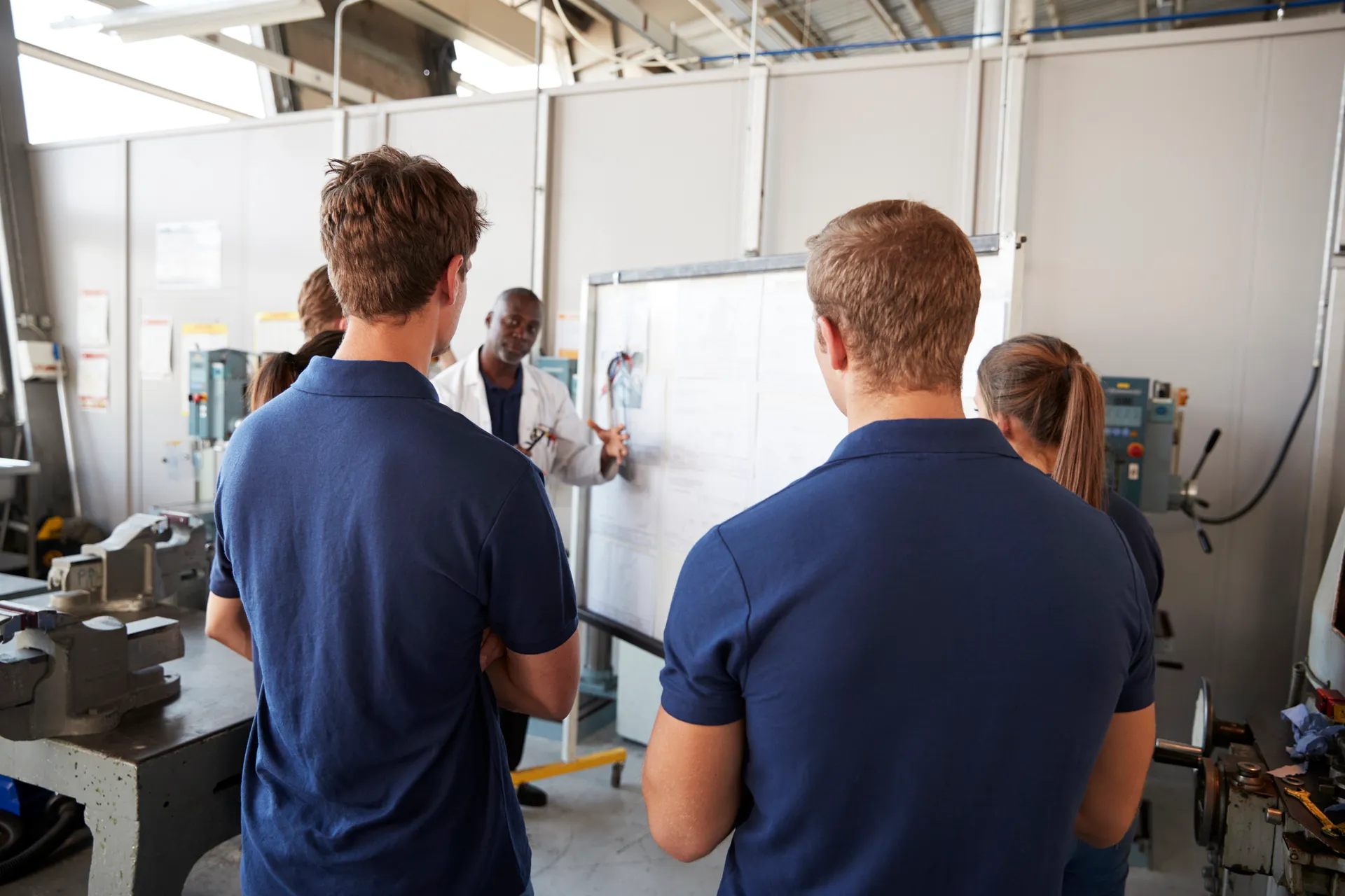 Several apprentices looking at employer showing notes and calculations on a whiteboard