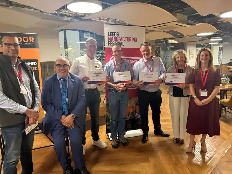 7 people holding certificates posed in front of roller banners displaying Leeds Manufacturing Festival