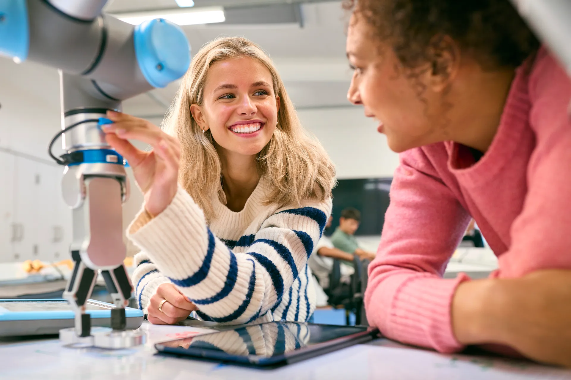 Two Female College Or University Engineering Students Using Digital Tablet To Control Robot Arm