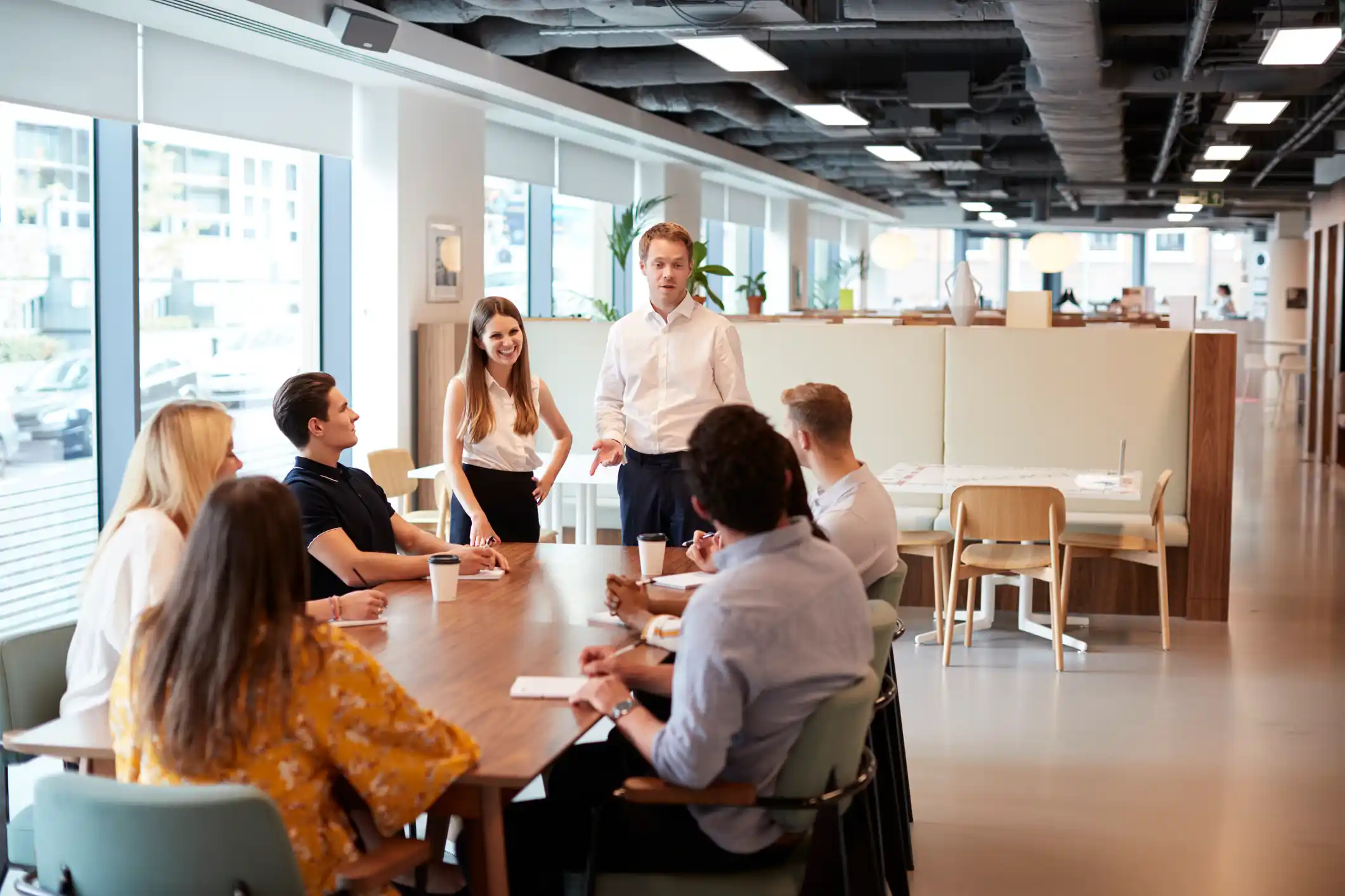 Businessman And Businesswoman Addressing Group Of Young Candidates Sitting Around Table And Collaborating On Task At Graduate Recruitment Assessment Day