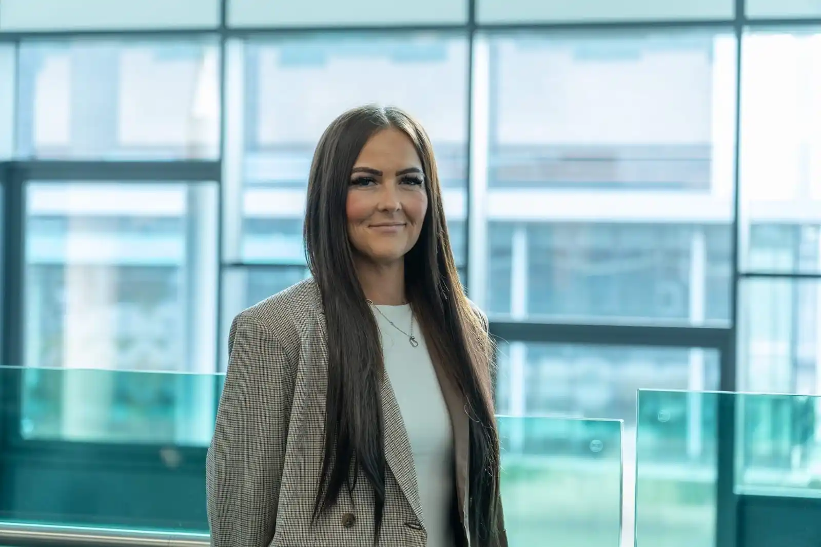 photo of Rachel Knowles, a woman with long brown hair wearing a light brown jacket, standing in front of a window