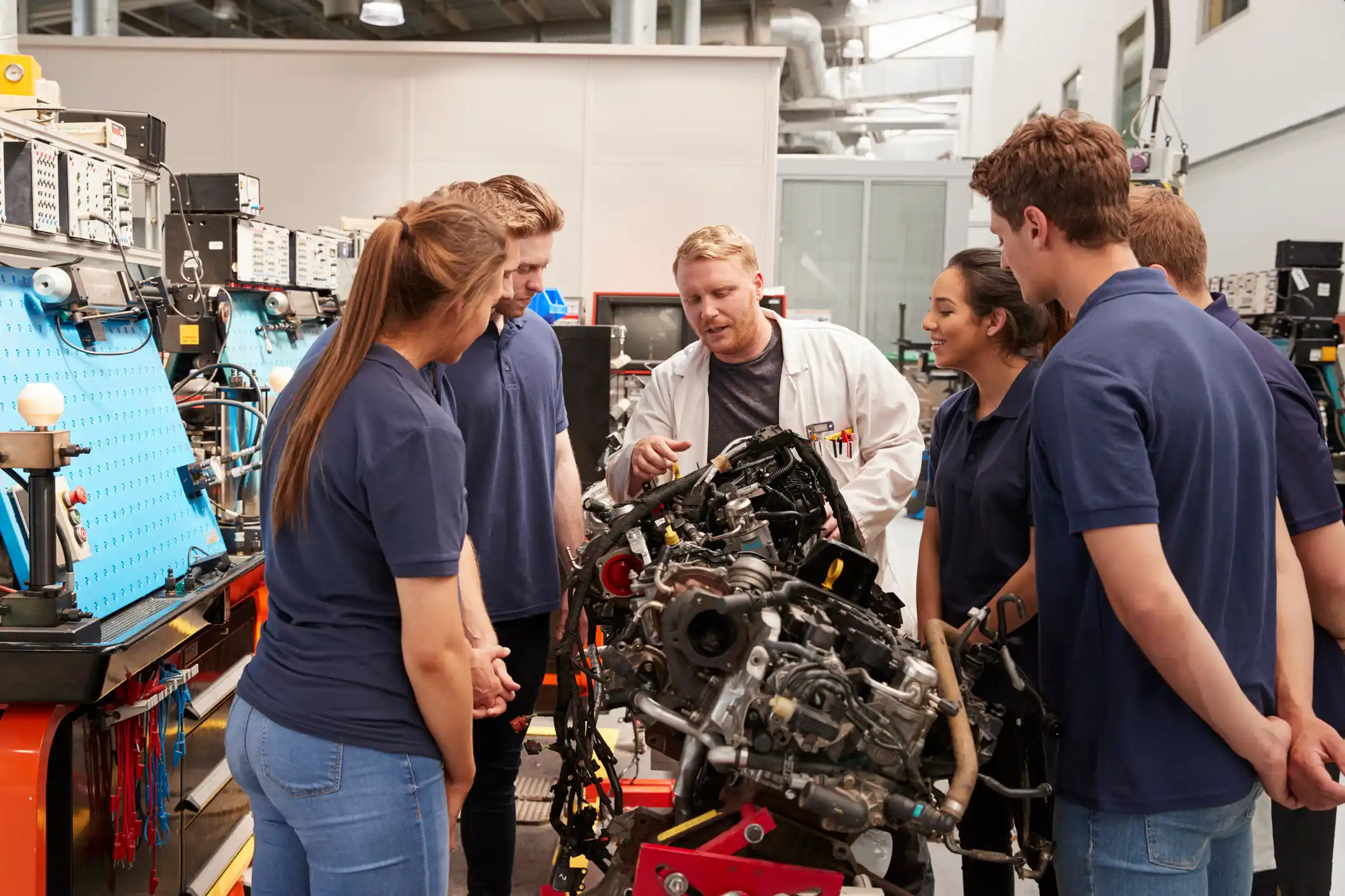 Apprentices looking at a car engine in a workshop.