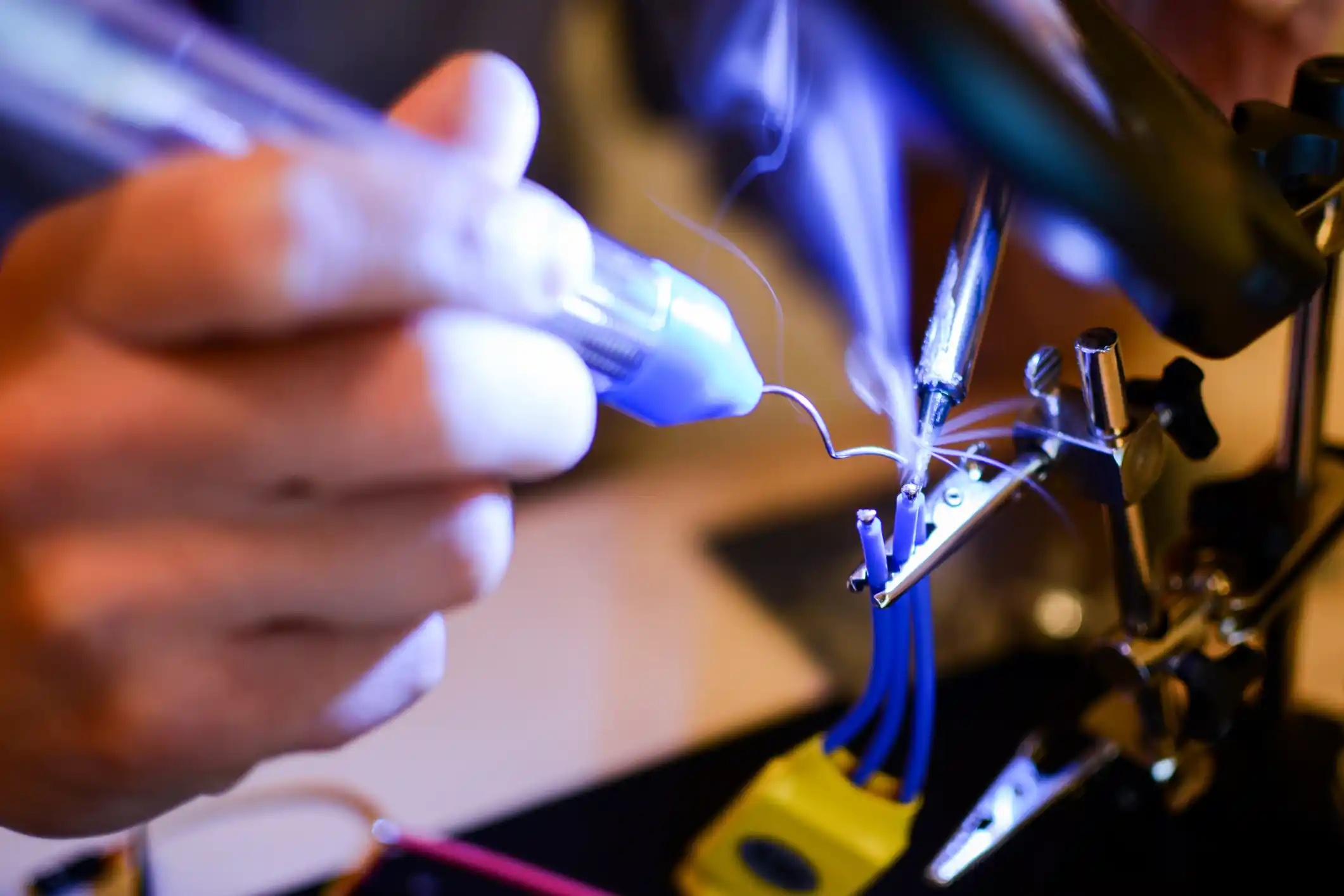 Smoke appears while soldering ESC and rotor wires with helper hands. Technology and electrical engineering concept
