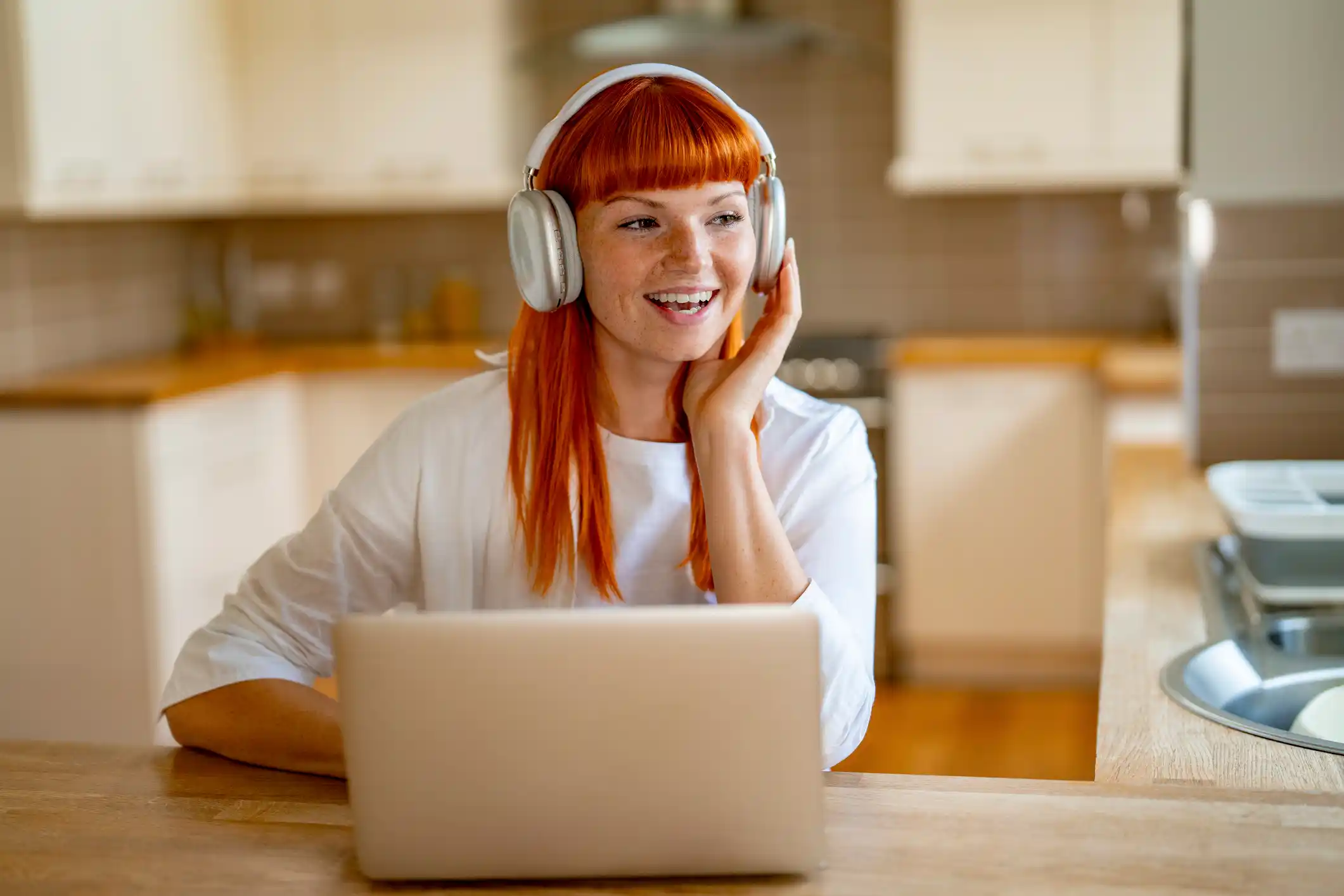 Cheerful Woman Enjoying Music While Working on Her Laptop in a Bright Kitchen