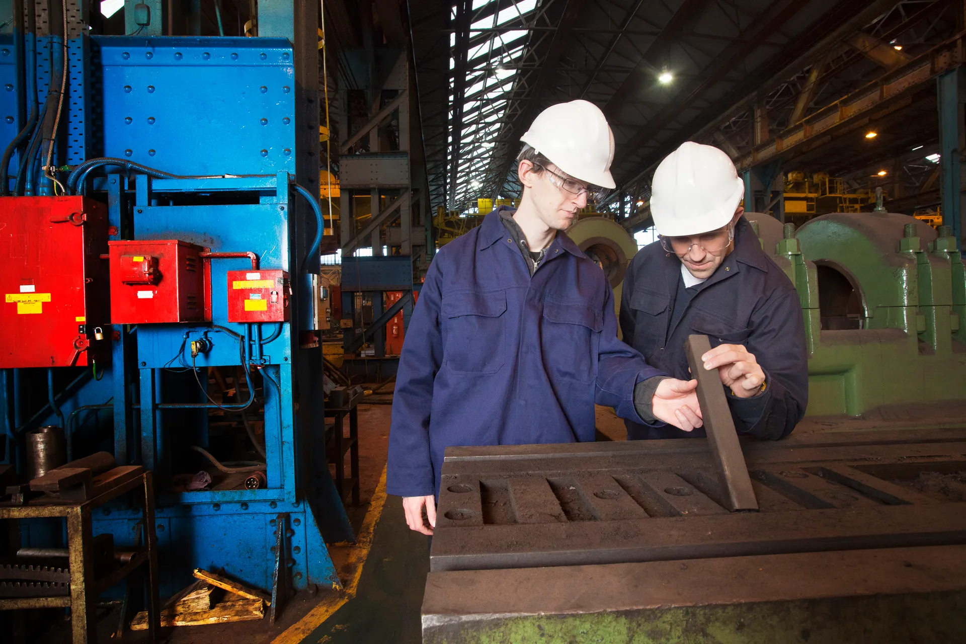 Workers examining metal in steel forge