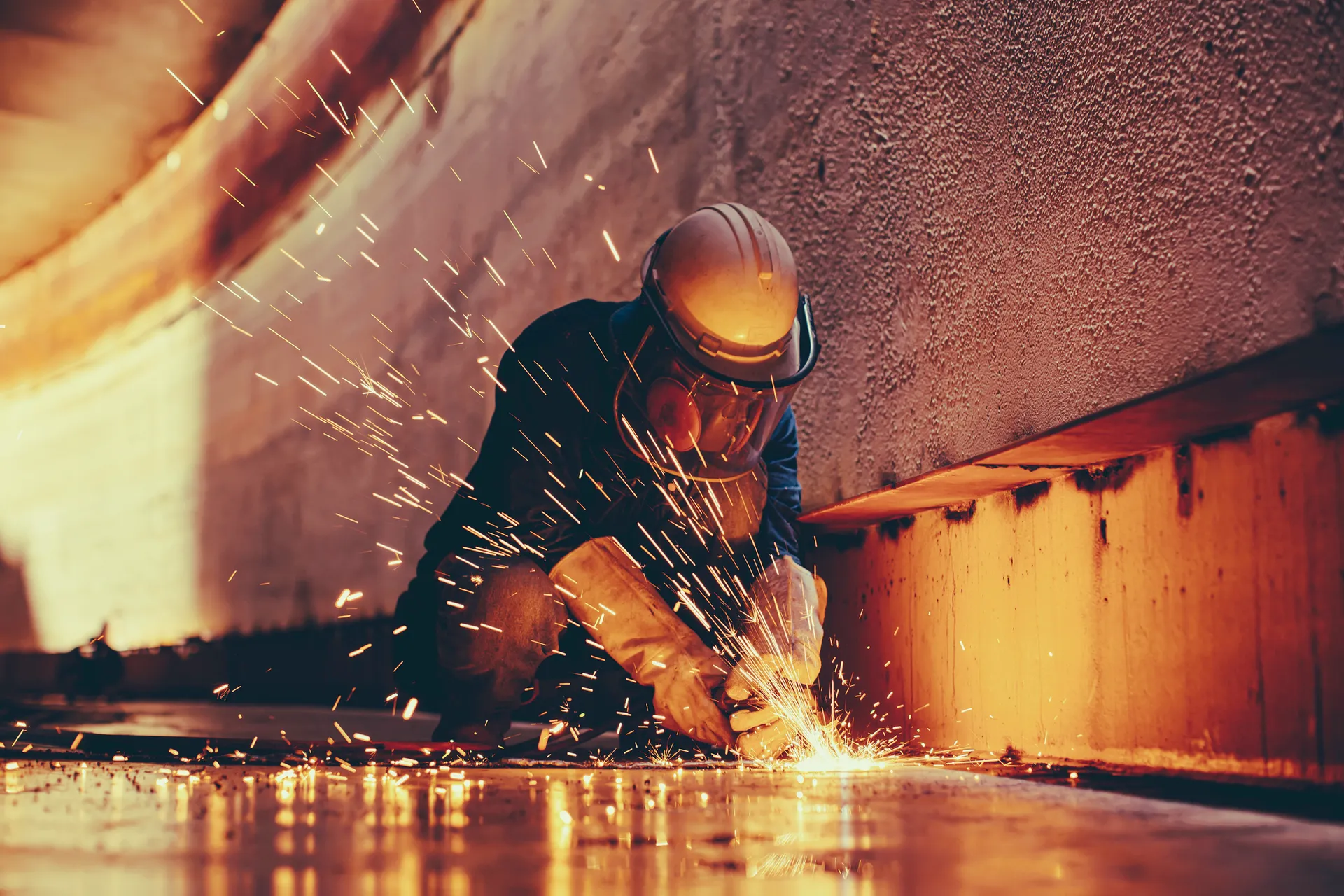 Male worker metal cutting spark on tank bottom steel plate with flash of cutting light close up wear protective gloves and mask