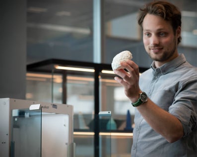 A man looks at a white, 3D printed object in his left hand