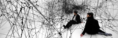  Two men sit in a gigantic black spider web (sculpture by Tomas Saraceno)
