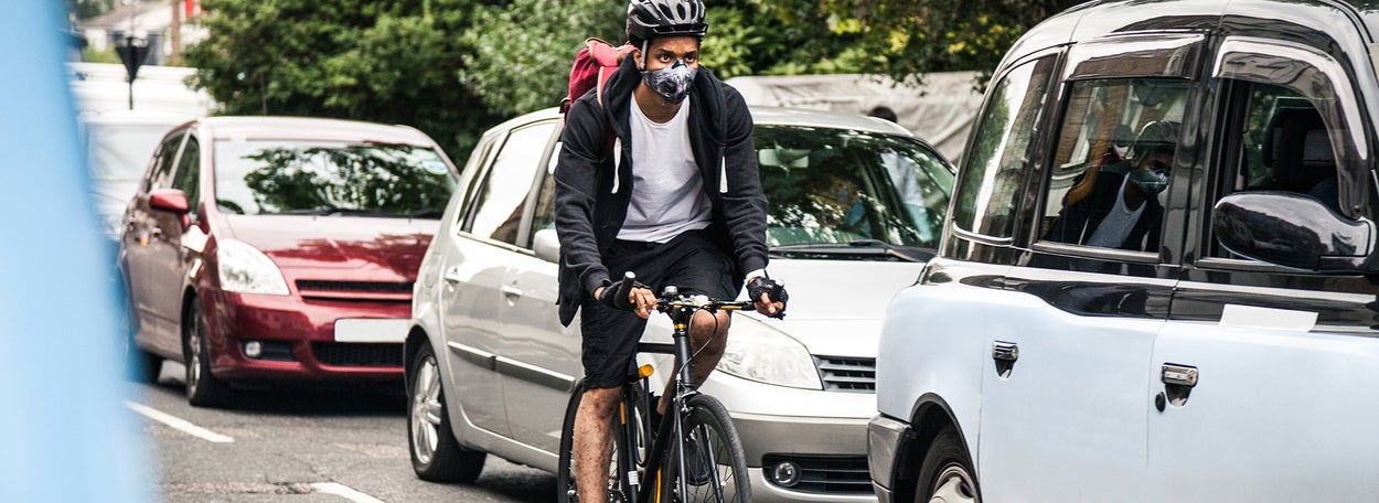 Fietser fietst met een mondkapje op naast auto's 
