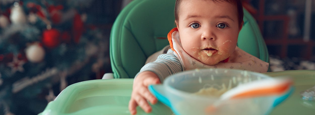Baby met etensresten om de mond houdt bordje met eten vast