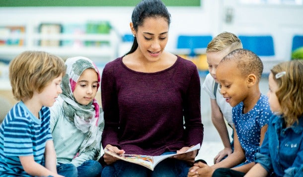 Vrouw leest voor te midden van vijf basisschool kinderen.