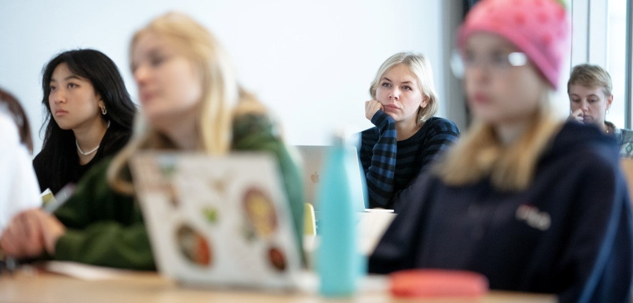 Students at tables with laptops looking intently in the same direction, except for one