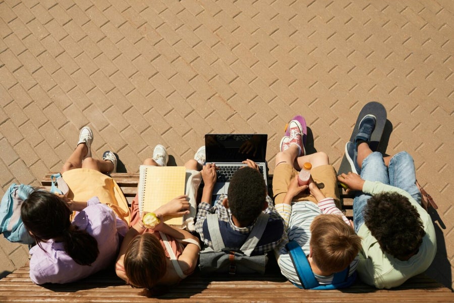 Children sitting on a bench with an apple or fruit juice in their hand.