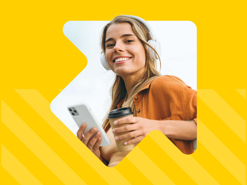 Een vrouw met een koptelefoon op en een telefoon en een kop koffie in de hand