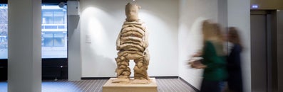 Het beeld De Zakkendraagster bestaat uit gestapelde juten zakken gevuld met zand en vormt een enigszins uitgezakte figuur. De jute vergaat, waardoor het zand heel langzaam wegstroomt, totdat er geen hij of zij meer overblijft. Het beeld staat min of meer op de uitkijk op een centrale plek in het hoofdgebouw van de VU. © Rene den Engelsman