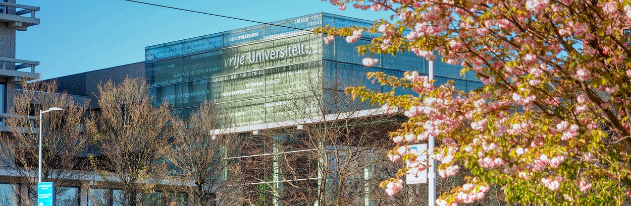 VU Hoofdgebouw in de de zon in het voorjaar met roze bloesemboom.
