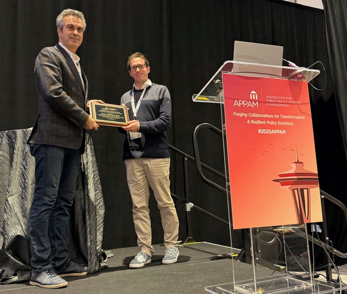 A man holds a plaque with a man next to a podium