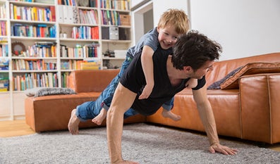 Zoontje rijdt in de woonkamer paard op de rug van papa