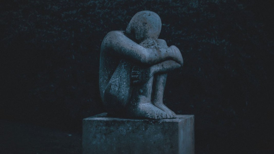 beeld van verdrietige, zittende man met armen om benen heen