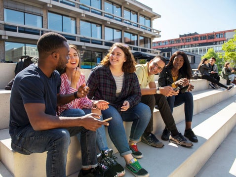 Vier studenten die met elkaar praten, zittend op een trap op het campusplein