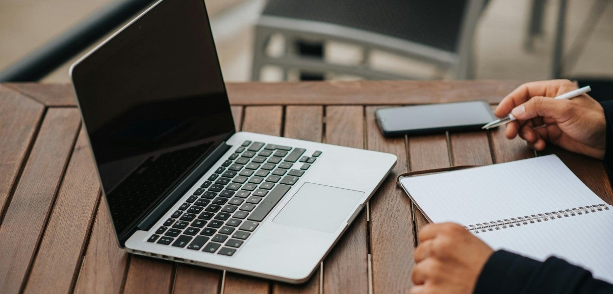 Person writing notes with a laptop in front of them