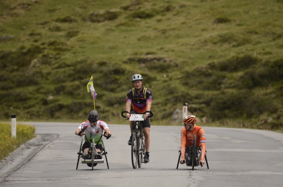 A participant of the HandbikeBattle encourged by Paralympic champion Mitch Valize and a companion on a bike.