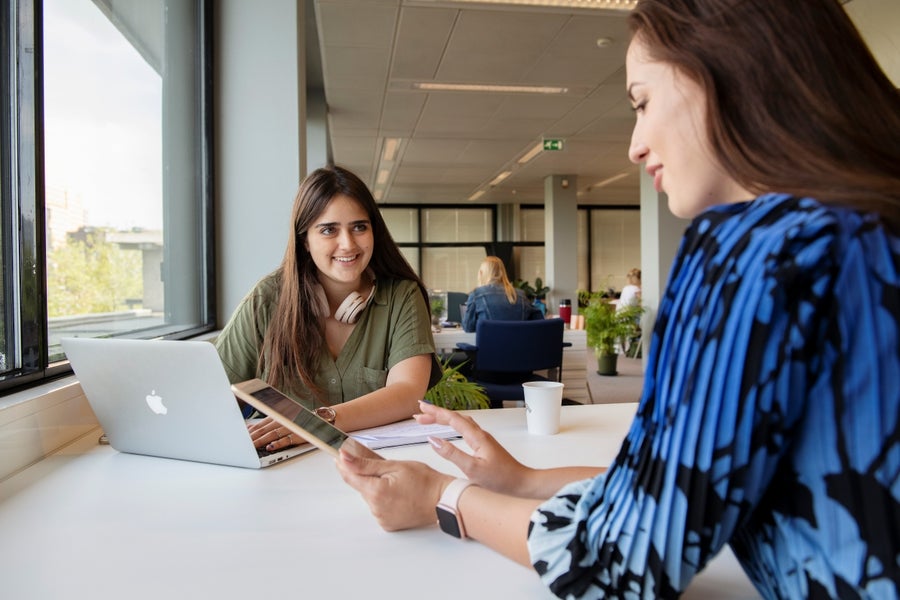 Docent en student aan een tafel, zijn in gesprek met elkaar en maken notities