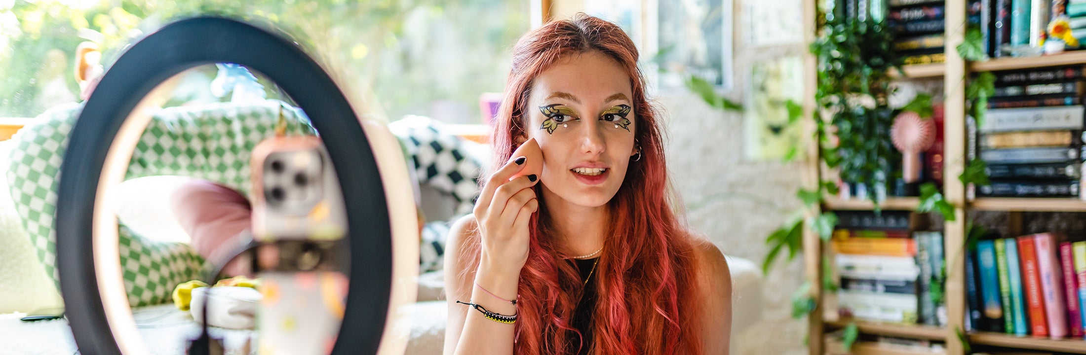 Een jonge vrouwelijke influencer verzorgt haar kleurrijke make-up terwijl ze een opname maakt.