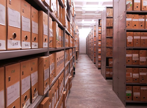 A storeroom with rows of shelves containing light brown filing boxes with white lettering.