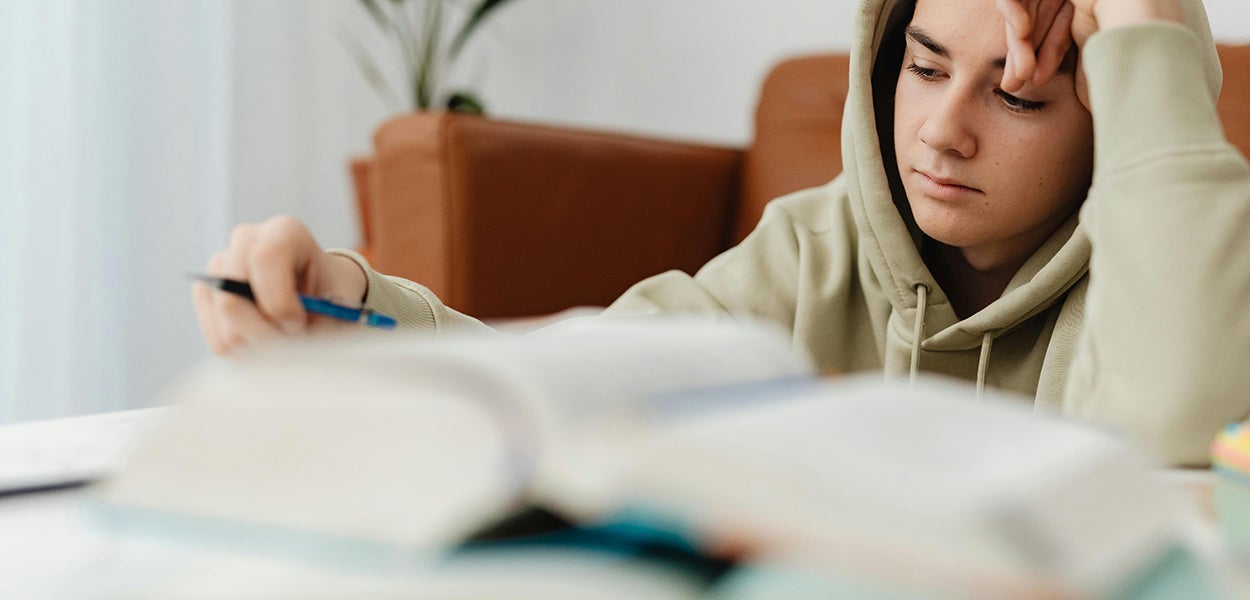 Een tiener is aan de studie aan een tafel met een groot boek voor zich