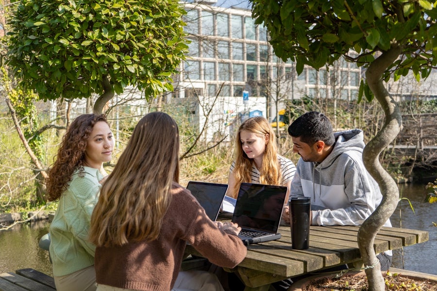 Vier studenten met laptops aan een tafel in de tuin van de VU