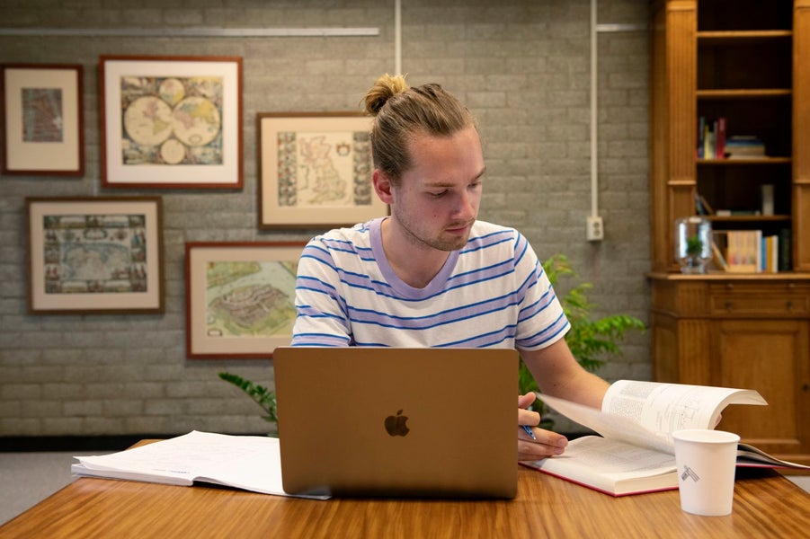 Een man aan een bureau met een laptop en een boek