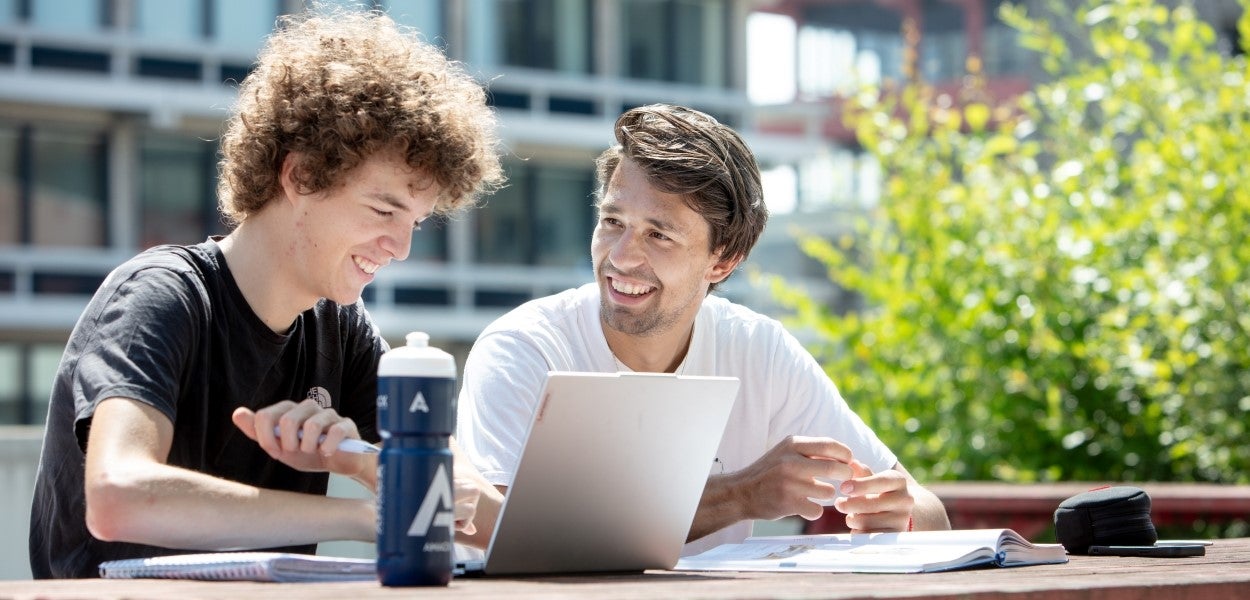 Two students talking to each other outside at a table