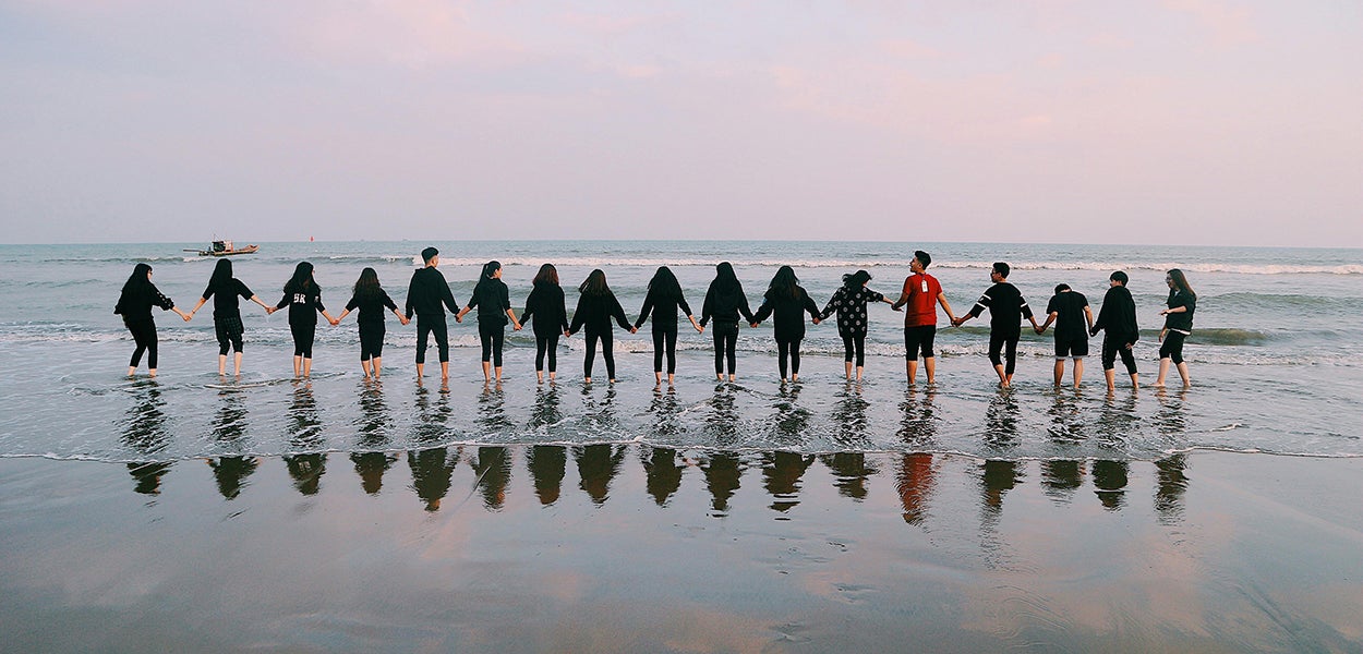 Een groep mensen staat als een team hand in hand in de zee. 