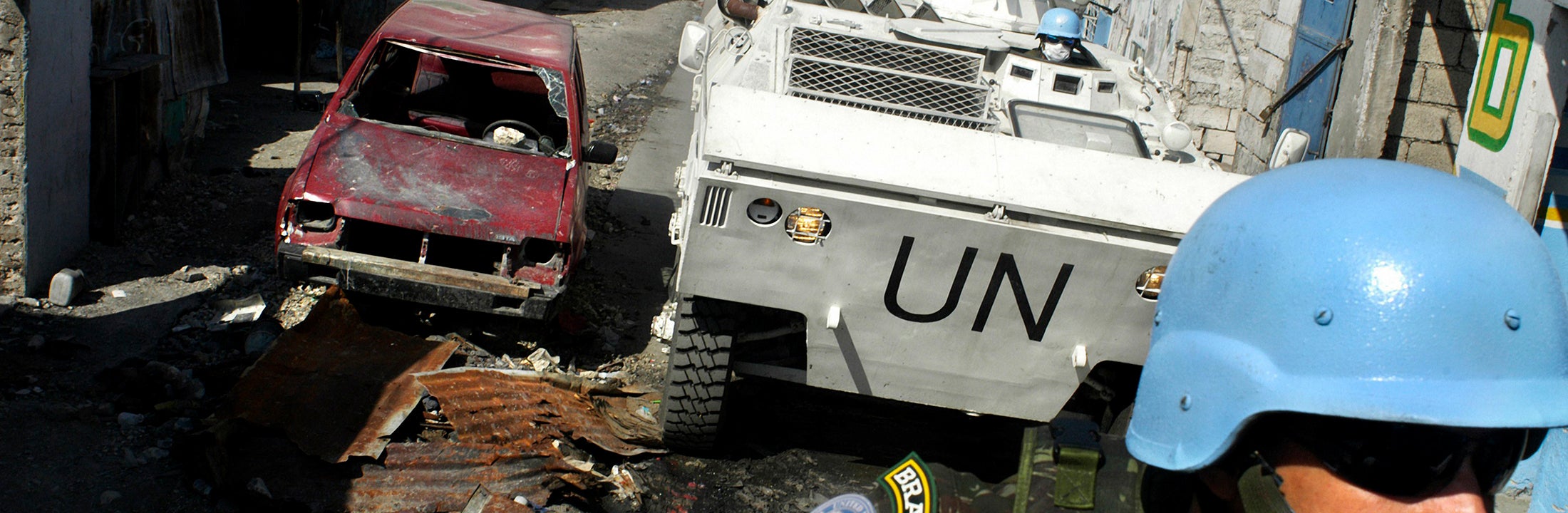 A blue helmet soldier looks towards moving UN tank