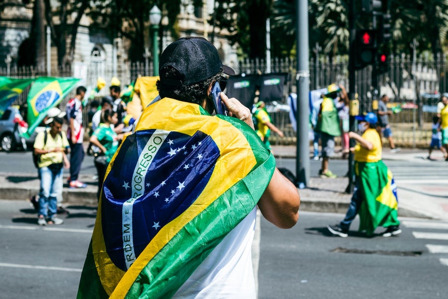 A protester draped in the Brazilian flag, talking on the phone in the street.