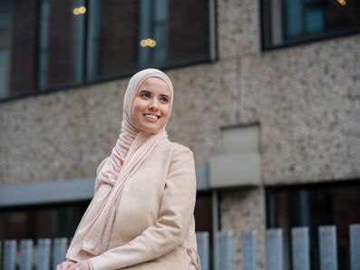Een vrouw met een hoofddoek staat buiten een gebouw