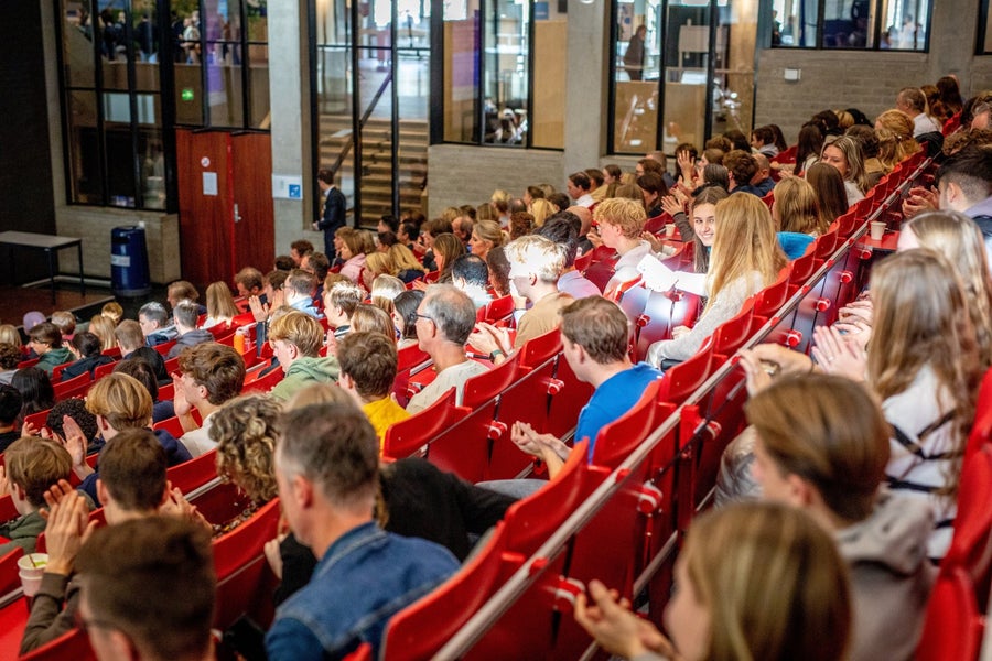 A lecture hall full of people sitting on red benches
