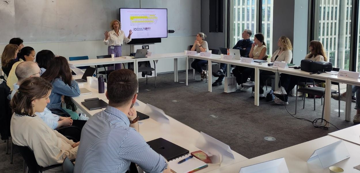 A group of researchers sitting at tables in a room with a large screen