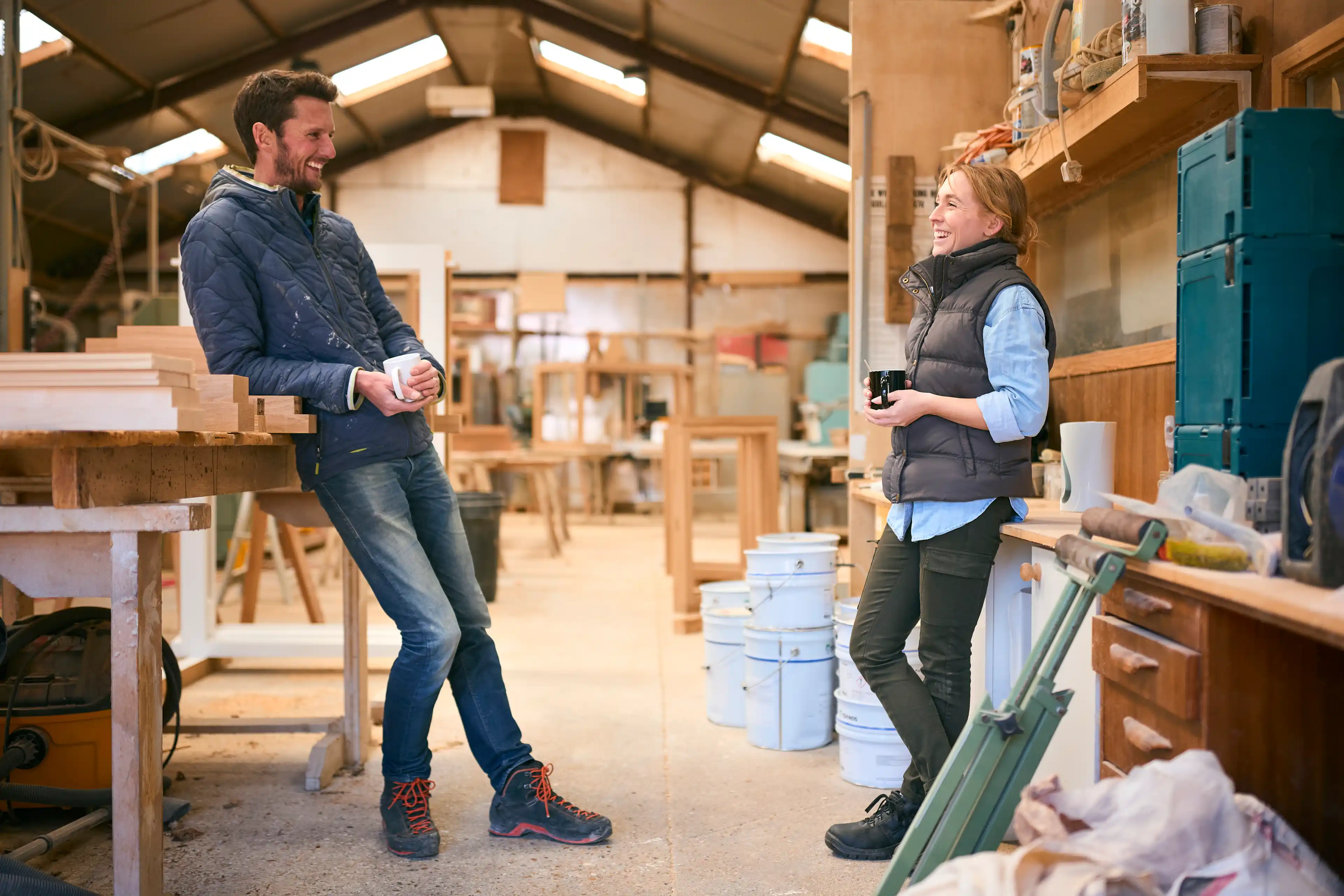 Male And Female Carpenter Working In Woodwork Workshop Talking On Coffee Break