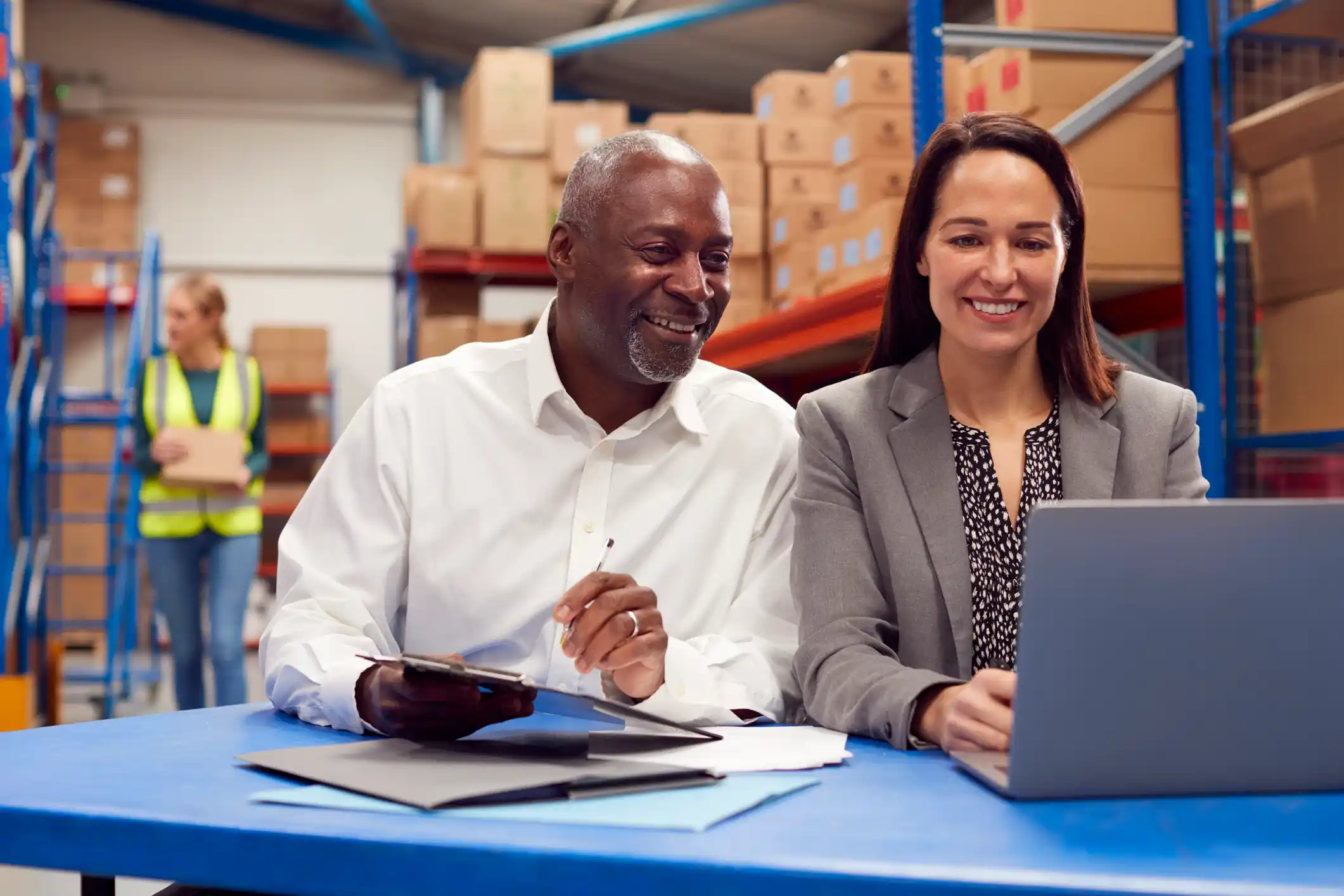 A man and woman in a warehouse setting, looking at a laptop