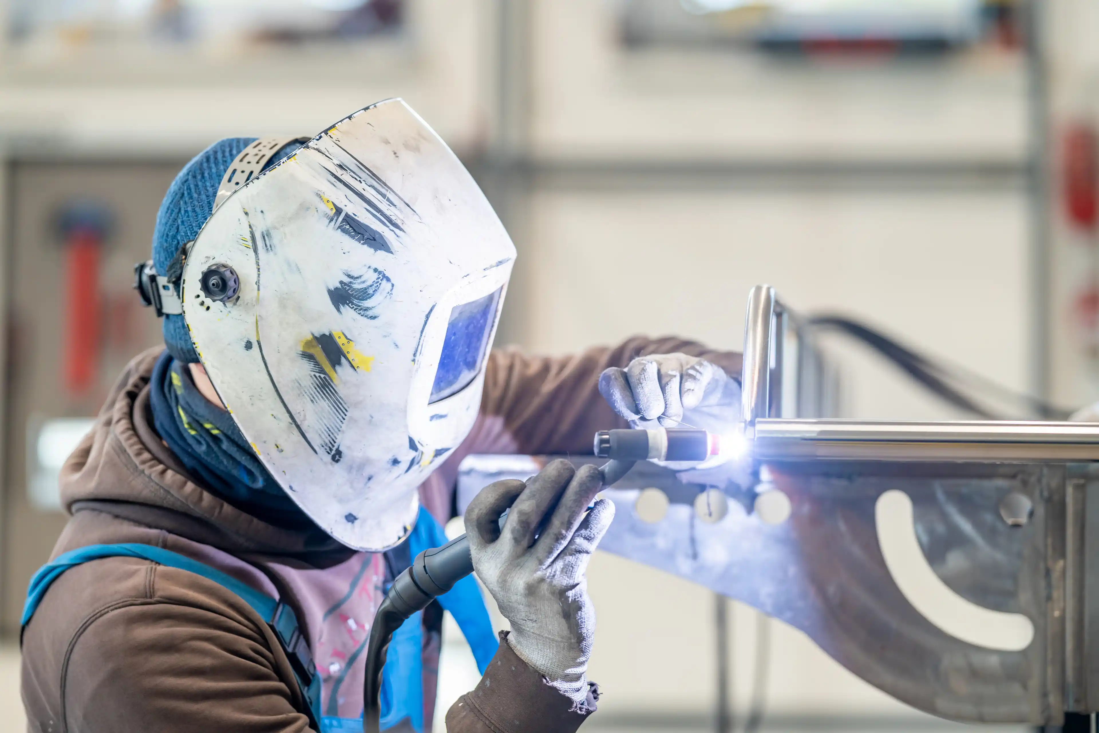 A man in personal protective equipment is welding metal in a factory stock photo