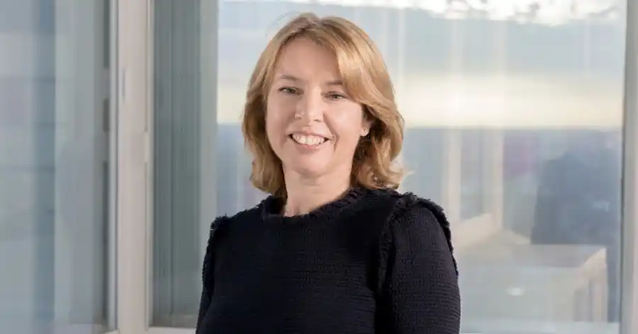 Sharron Pamplin in black shirt smiling at camera in front of glass windows