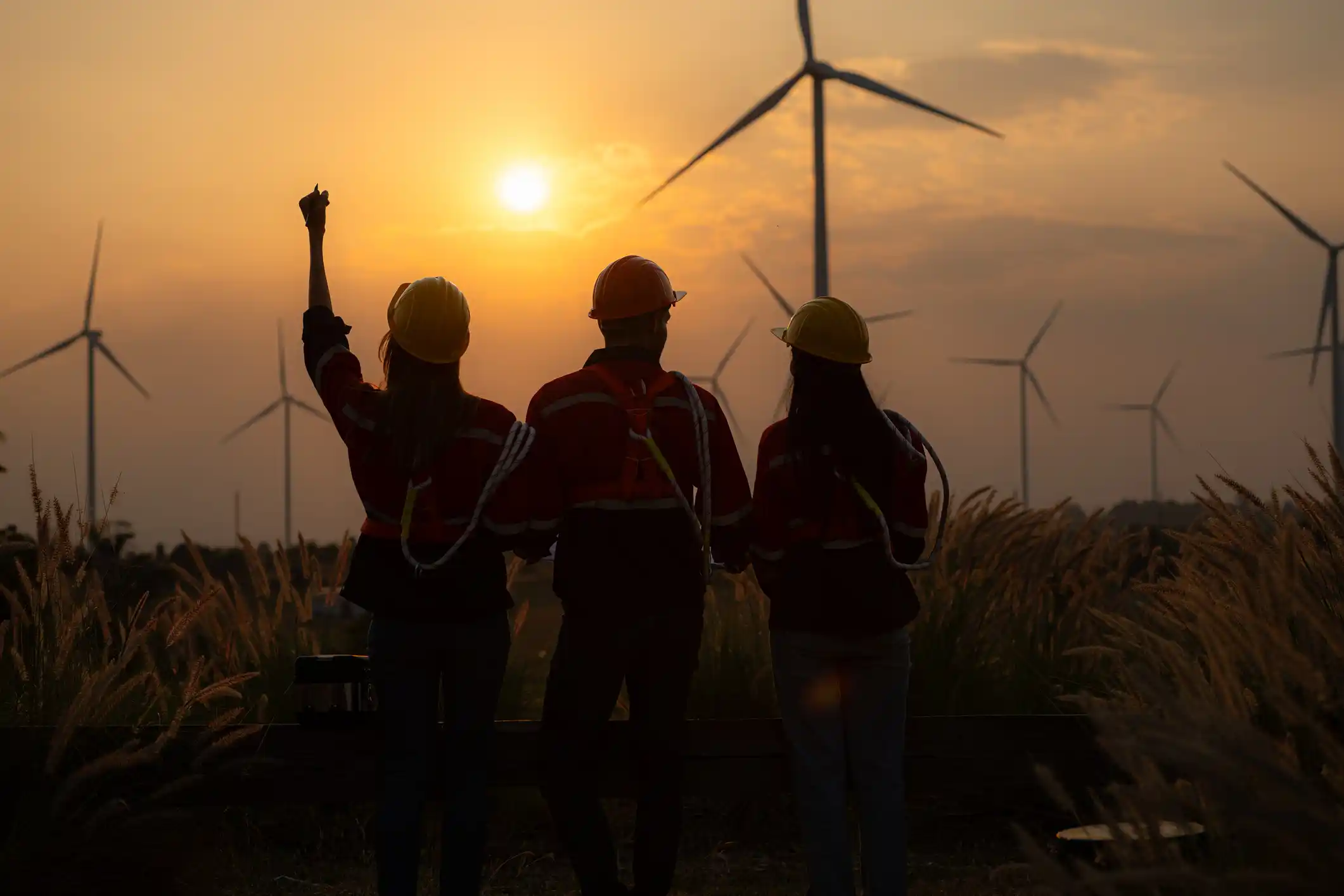 Silhouette of a group of engineers and windmills on the background of a sunset. 