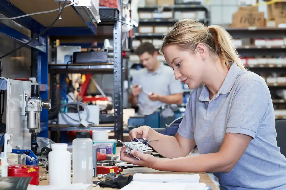 Female Engineer In Factory Measuring Component At Work Bench Using Micrometer