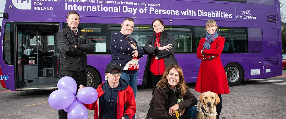 People stand in front of a bus wrapped for purple lights